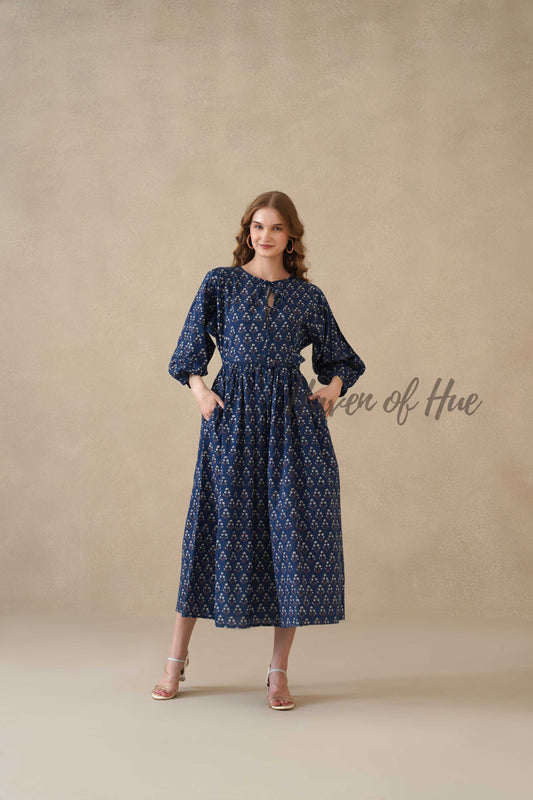 A woman standing in a serene sky blue long sleeve cotton midi dress with a white floral botanical print.