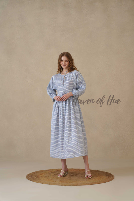 A woman standing in a serene blue and white full sleeve cotton midi dress with a geometric teardrop print.